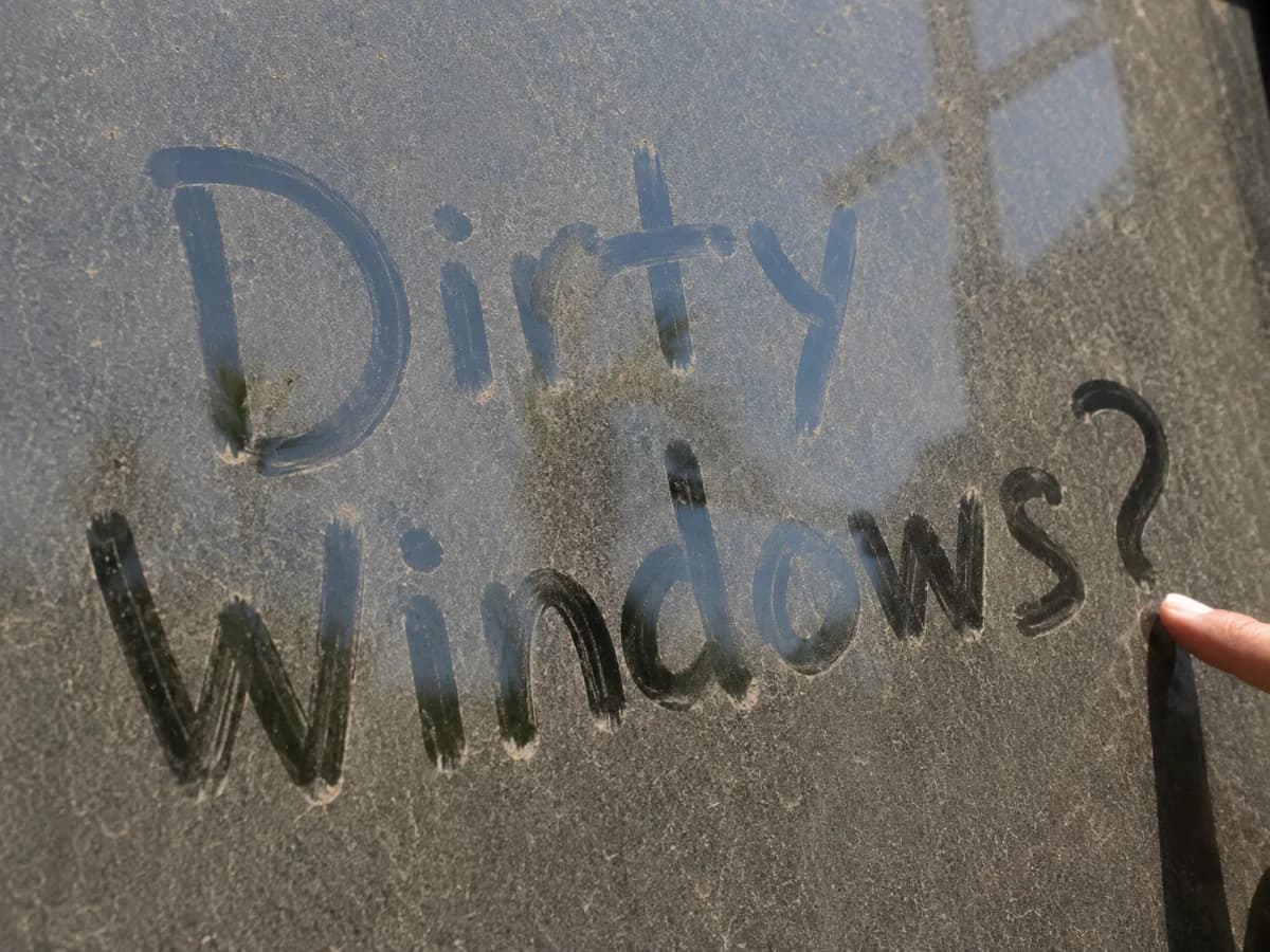 Grimy window with โDirty Windows?โ finger-written in the dust